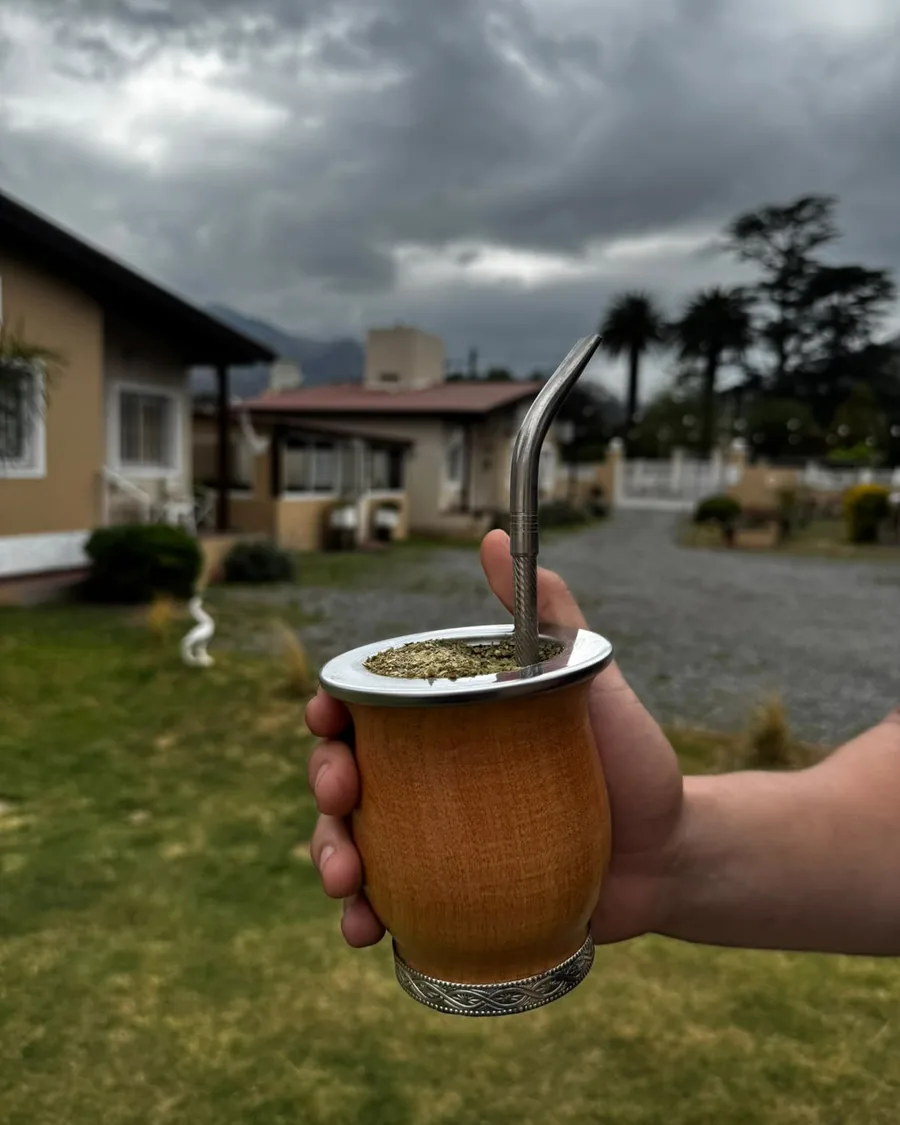 Mate de madera con virola de acero y bombilla, en la mano, con yerba